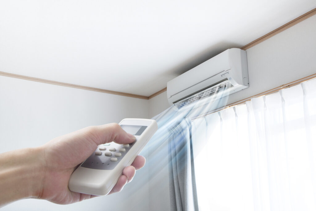 Ductless mini-split installed high on wall with person's hand pointing remote control at it.